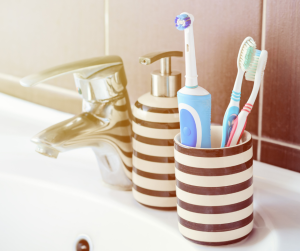 Electric and Manual Toothbrushes in Cup on Bathroom Sink