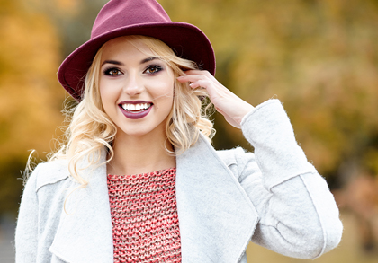 Blonde woman wearing a cranberry hat amd smiling, for information on porcelain veneers